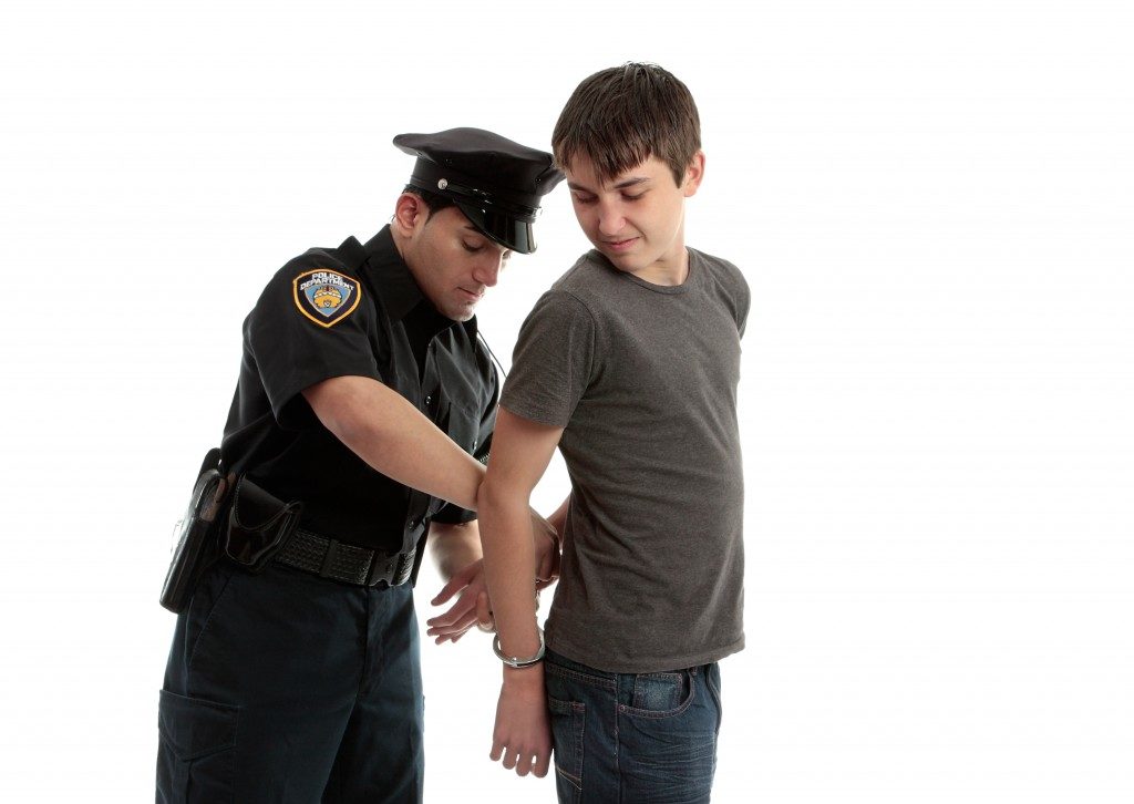 A police officer arrests and handcuffs a young male teen