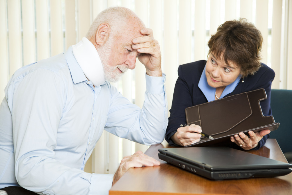 An old man with a neck brace talking to a lawyer in an office