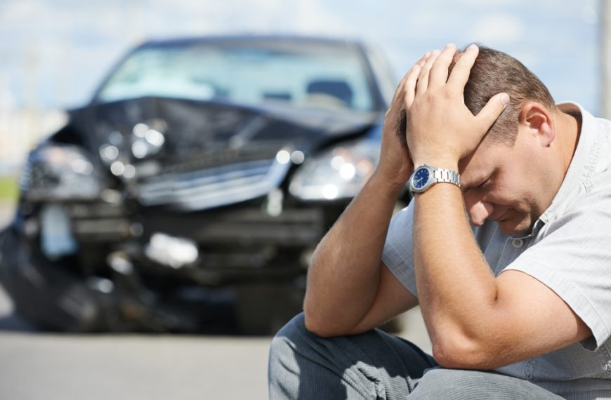 A stressed man, with his hands on his head, worried about a crashed car