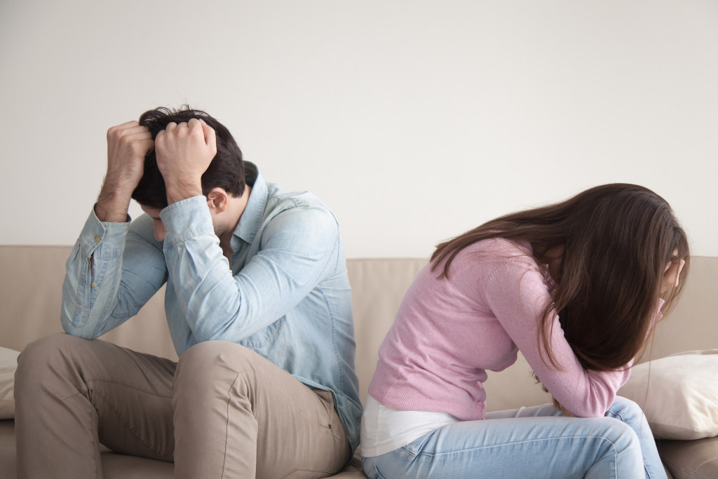frustrated and sad couple in opposite sides of a living room couch