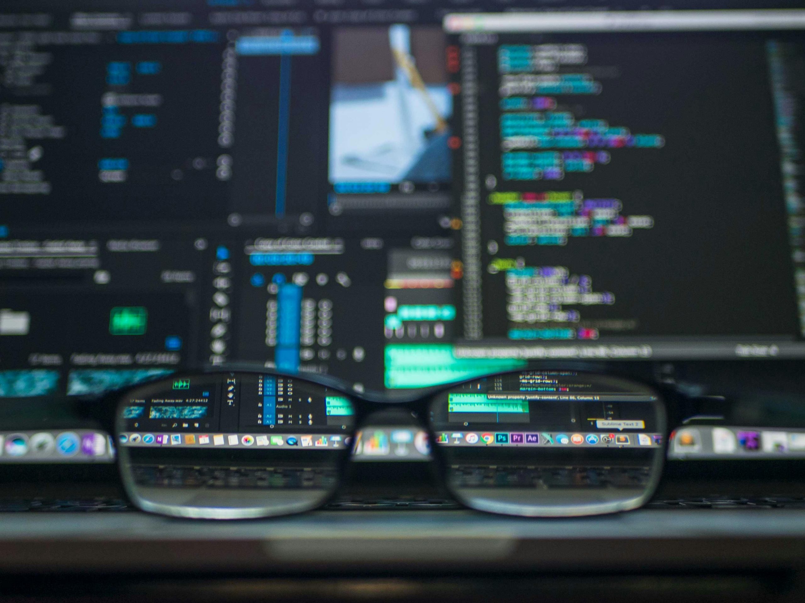 eyeglasses resting on a laptop keyboard, with the screen visible and filled with programming code