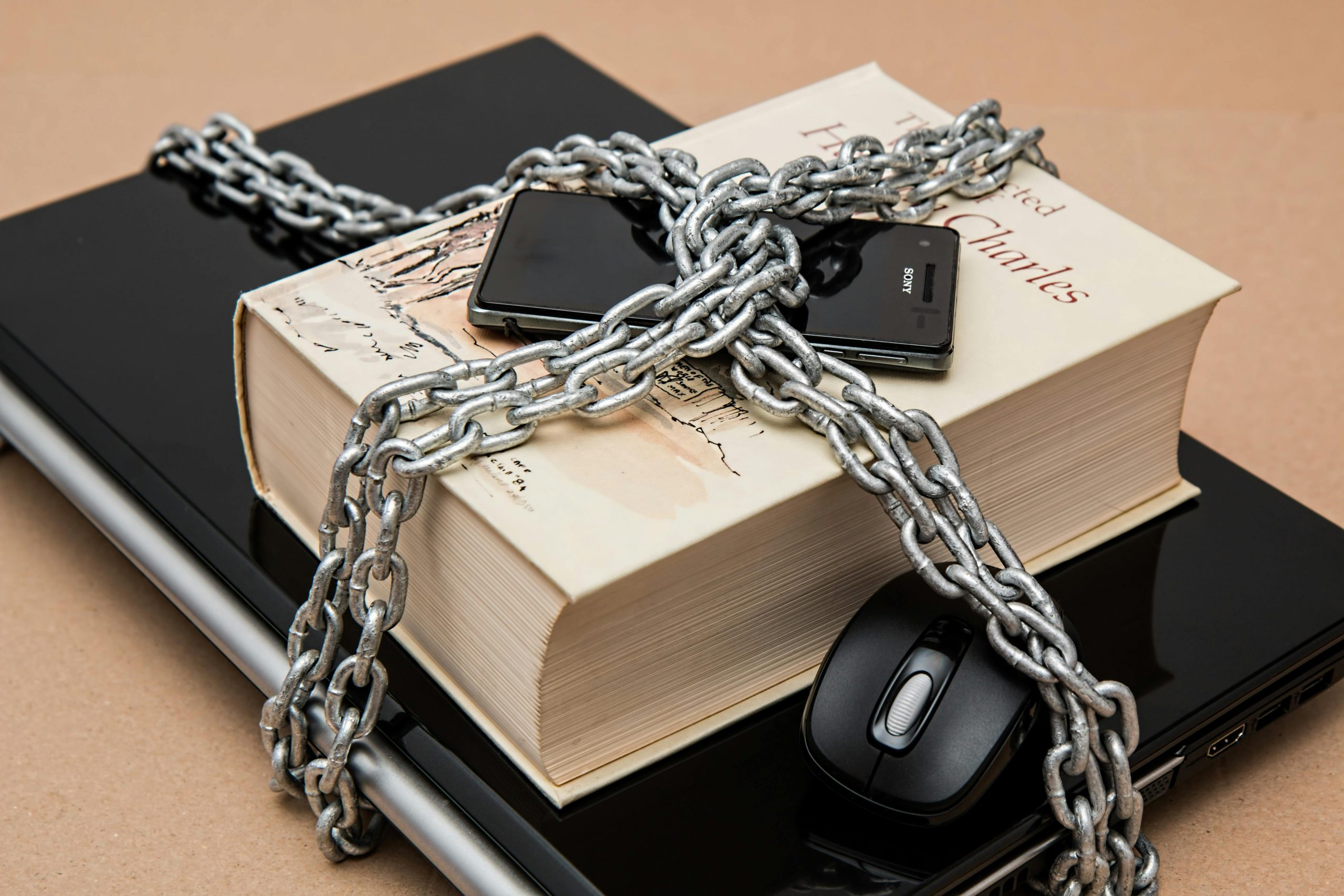 laptop, book, smartphone, and computer mouse bound in metal chains