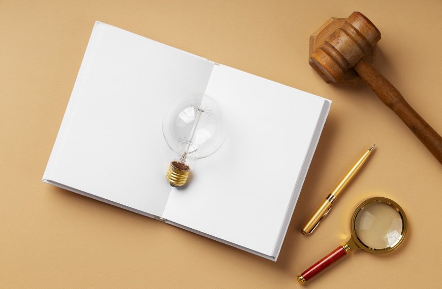open book with a light bulb on top, gavel, pen, and magnifying glass on a wooden table