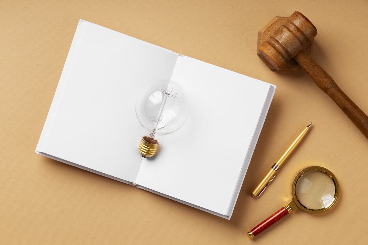 open book with a light bulb on top, gavel, pen, and magnifying glass on a wooden table